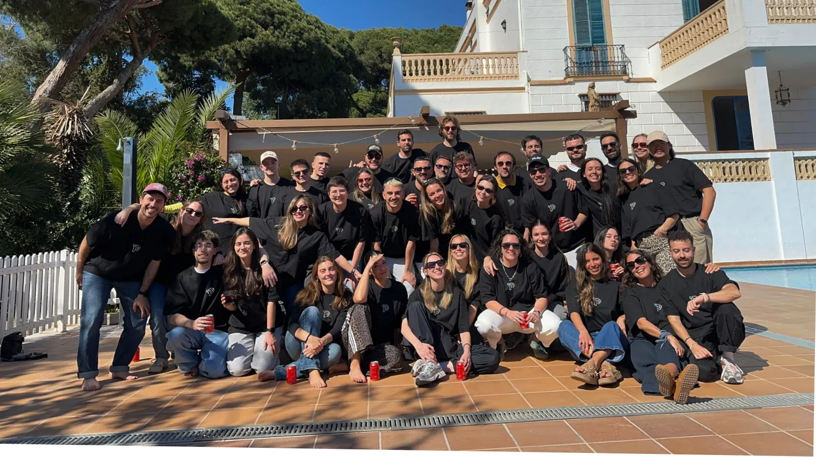 El equipo de PlayYourBrand reunido al aire libre, con camisetas negras de PLAY, frente a una villa con piscina.